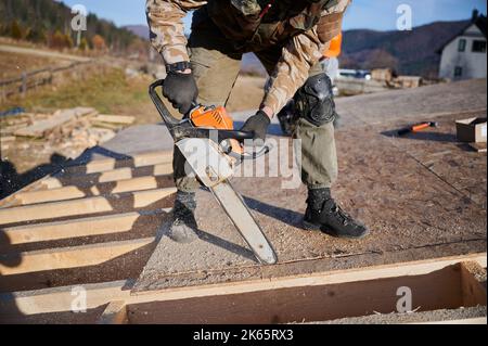 Menuisier utilisant une tronçonneuse pour couper des panneaux OSB en bois. Homme ouvrier bâtiment maison de cadre en bois sur la base de pile. Concept de menuiserie. Banque D'Images