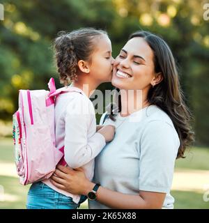 Adorable petite fille embrassant sa mère sur la joue à l'extérieur. Adorable enfant de race mixte disant Au revoir à un parent à l'extérieur avant d'aller à l'école Banque D'Images