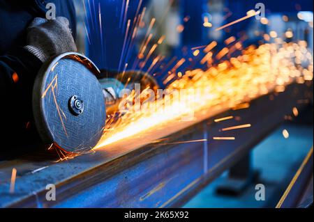 Un ouvrier coupe une poutre métallique avec un disque abrasif en atelier Banque D'Images