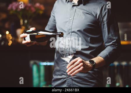 L'homme verse du vin blanc dans un verre à vin dans un restaurant semi-sombre Banque D'Images