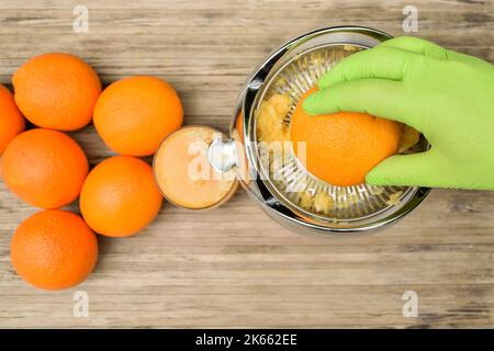 Vue de dessus d'une main dans un gant de protection lors de la préparation du jus d'orange à l'aide d'un presse-agrumes électrique Banque D'Images