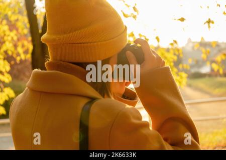 Une femme dans un chapeau orange et un manteau brun photographie le parc d'automne, vue arrière. Banque D'Images