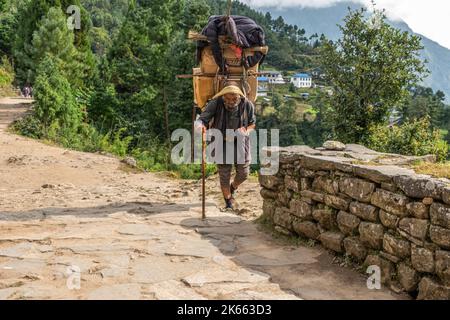 Sherpa âgé avec bâton, transportant une lourde charge sur l'Everest Way Népal Banque D'Images