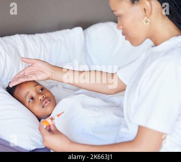 Femme afro-américaine prenant la température de son fils. Mère utilisant un thermomètre pour mesurer la température des fils. Petit garçon malade allongé dans le lit. Inquiet Banque D'Images