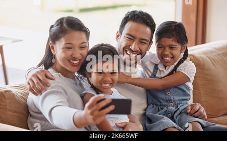 Selfies avec toute la famille. Une jeune famille affectueuse de quatre personnes prenant des selfies sur le canapé à la maison. Banque D'Images