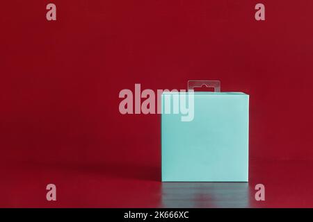 Une boîte en carton vierge carrée bleue sur un arrière-plan de studio rouge coloré avec espace de copie. Concept de cadeau, de livraison et d'expédition. Banque D'Images