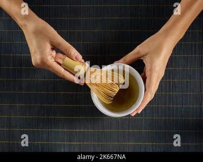 Les mains préparant le thé matcha dans un bol blanc avec un fouet en bambou Banque D'Images