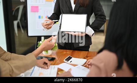 Une femme d'affaires ou un patron professionnel forme son personnel lors de la réunion, présentant ou affichant quelque chose sur l'écran d'une tablette, en tenant une tablette Banque D'Images