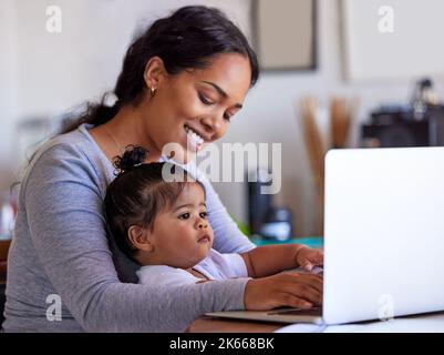 Mère et bébé travaillant à la maison, à l'aide d'un ordinateur portable. Une jeune femme qui navigue en ligne sur un ordinateur tandis que sa petite fille mignonne est assise sur ses genoux. Bonne maman Banque D'Images