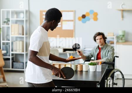 Portrait d'un jeune homme noir jouant au tennis de table au bureau contre un collègue handicapé, concept d'inclusivité en milieu de travail Banque D'Images