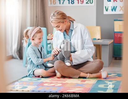 Jeune pédiatre caucasien aidant une petite fille à écouter le battement de coeur d'un jouet avec un stéthoscope. Petit enfant heureux en visite chez le médecin pour un Banque D'Images