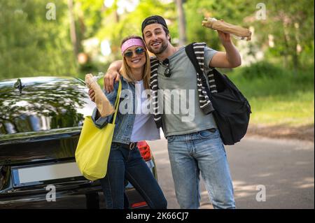Un jeune couple mignon qui a l'air excité et joyeux debout près de la voiture Banque D'Images