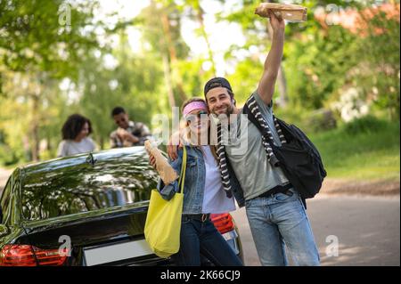 Un jeune couple mignon qui a l'air excité et joyeux debout près de la voiture Banque D'Images