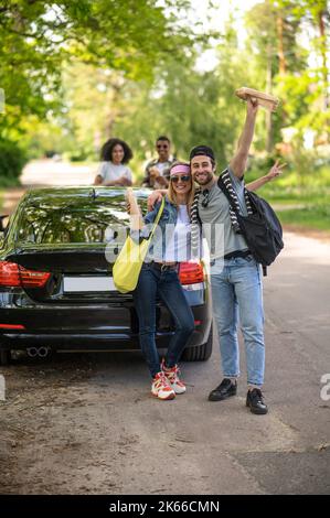 Un jeune couple mignon qui a l'air excité et joyeux debout près de la voiture Banque D'Images