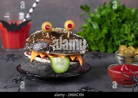 Sandwich monstre avec pain noir, saucisse, fromage, concombre et yeux d'olive sur fond marron Banque D'Images