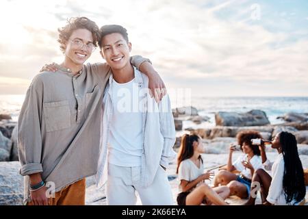 Portrait de deux jeunes hommes attrayants debout ensemble sur la plage. Un homme asiatique et son meilleur ami s'embrassant lors d'une journée avec des amis Banque D'Images