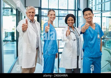 Qui n'aime pas les soins de santé. Un groupe de médecins montrant un pouce vers le haut dans un hôpital moderne. Banque D'Images