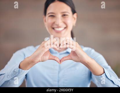 Souriante femme d'affaires de race mixte debout seul et utilisant des gestes de main pour faire une forme de coeur. Professionnel plein de confiance et ambitieux Banque D'Images