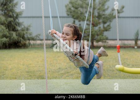 Portrait de balançoires de fille gaie sur balançoire en osier pour marcher dehors le jour ensoleillé d'été. Émotions joyeuses. Joie de l'enfance. . Photo de haute qualité Banque D'Images