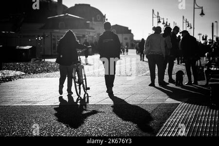 Les gens marchent sous le soleil de la fin de l'après-midi sur le front de mer de Worthing, West Sussex, Royaume-Uni. Banque D'Images