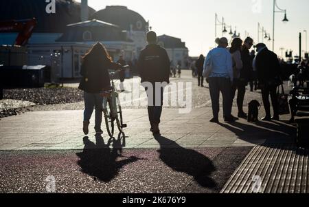 Les gens marchent sous le soleil de la fin de l'après-midi sur le front de mer de Worthing, West Sussex, Royaume-Uni. Banque D'Images