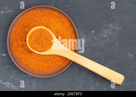 Épice au piment rouge dans une assiette en argile et cuillère en bois sur fond de béton noir. Macro. Vue de dessus. Concept de cuisine végétarienne Banque D'Images