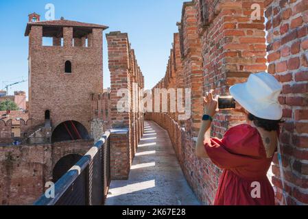 Touriste féminin, vue arrière en été d'une jeune touriste femelle prenant une photo des murs de la forteresse de Castelvecchio à Vérone, Italie. Banque D'Images