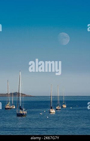 89% de Hunters illuminés Lune qui s'élève au-dessus des voiliers amarrés avec petite île en arrière-plan Banque D'Images