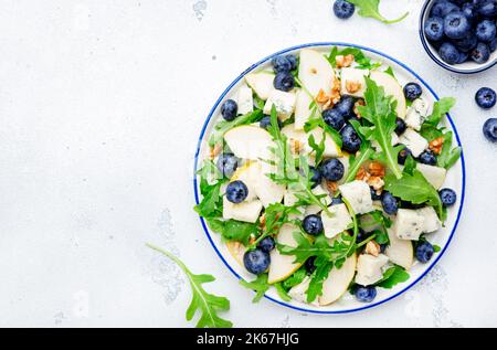 Delicious arugula salad with pears, blueberries, roquefort cheese and walnuts. Black kitchen table background, top view Banque D'Images