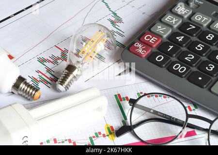 Gros plan des ampoules, de la calculatrice et des lunettes à économie d'énergie sur le graphique imprimé. Concept pour l'augmentation du coût de l'électricité. Facture énergétique coûteuse et Banque D'Images