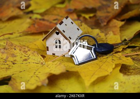Modèle de maison en bois et porte-clés sur fond de feuilles d'érable. Concept de chalet de campagne, recherche de logements en automne, immobilier Banque D'Images