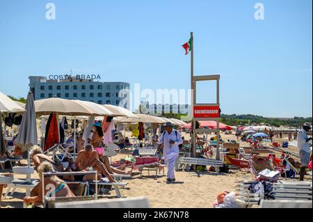 Un vendeur de plage se promène entre les baigneurs de soleil et les amateurs de plage sur la plage de Sottovento en essayant de vendre des colliers. Près de Gallipoli à Apulia (Puglia), Italie. Banque D'Images
