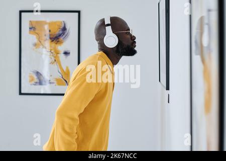 Un jeune homme africain dans un casque sans fil examine la peinture sur le mur à la galerie Banque D'Images