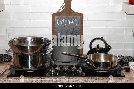 Casseroles et poêles sur un poêle noir dans une maison résidentielle prête à cuisiner un repas. Banque D'Images