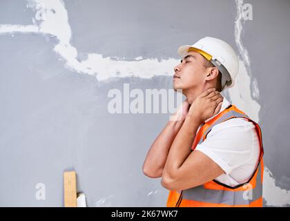 Un jeune ouvrier asiatique de la construction tient son cou dans la douleur de blessures de travail Banque D'Images