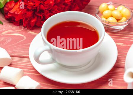 Tasse de thé avec bonbons et fleurs sur une table en bois Banque D'Images