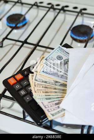 Paiement des factures de services publics, calculs sur une calculatrice. Les billets d'euro et de dollar sont près d'un brûleur à gaz en feu. Le concept d'augmenter le coût de Banque D'Images