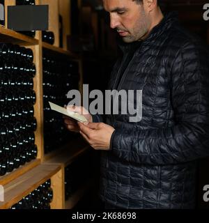 Homme dans la cave à vin avec des bouteilles en arrière-plan pour boire et déguster du vin. Banque D'Images