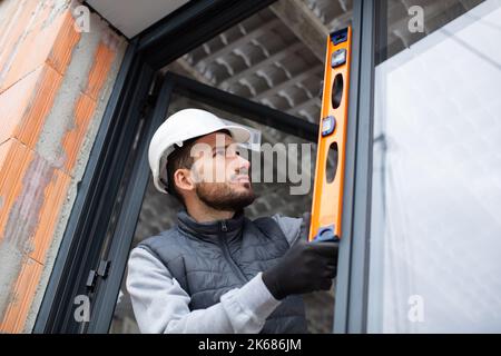 workman dans des fenêtres de montage uniformes en vérifiant leur niveau Banque D'Images