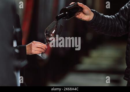 Homme versant un vin rouge dans un verre de femme pendant une dégustation dans une cave à vin, gros plan Banque D'Images