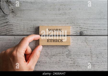 Main masculine assemblant un panneau d'éthique de travail écrit sur deux blocs de bois placés sur un fond en bois texturé. Banque D'Images