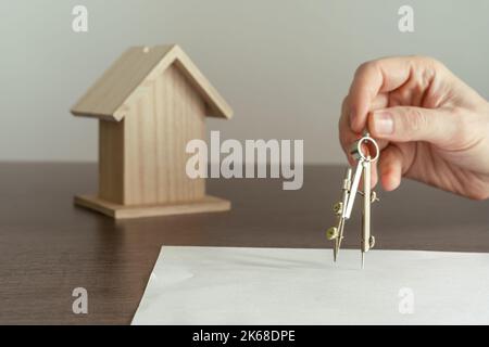 Architecte dessinant avec la boussole sur un livre blanc les plans d'une nouvelle maison pour une famille. Banque D'Images