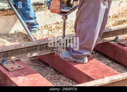 construction de voies ferrées avec traverses en bois. L'ouvrier avec un foret fait le trou dans lequel le boulon qui maintient le rail fixé sur le couchette Banque D'Images