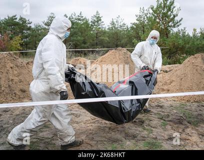 Les enquêteurs portant des engins de protection sont vus porter un sac de corps avec un corps soldat ukrainien qui a été exhumé d'un site d'enterrement à Lyman. Au moins 32 corps de soldats ukrainiens ont été exhumés d’une fosse commune de Lyman, une ville de la région de Donetsk qui était sous occupation russe. Les autorités ont déclaré qu'elles avaient été enterrées ensemble et l'enquête initiale a montré que certains corps étaient bandés et attachés aux mains, ce qui a suggéré des signes de torture et d'exécution. 22 autres civils, dont des enfants, ont été exhumés d'un autre lieu d'inhumation situé à proximité. Les deux sites sont situés au bord d'un cimètre Banque D'Images