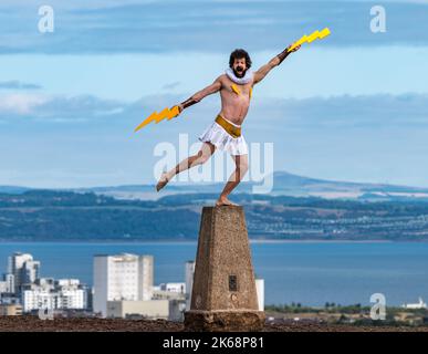 L'artiste de la frange Garry Starr aka Damien Warren-Smith comme Dieu grec Zeus avec des éclairs sur un point de trigpoint, Calton Hill, Édimbourg, Écosse, Royaume-Uni Banque D'Images