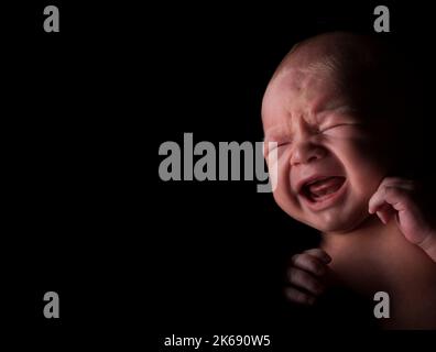 Bébé garçon avec une expression de pleurs dans un environnement sombre. Banque D'Images