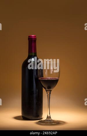 vue d'une bouteille de vin rouge et d'un verre contenant le même liquide, placé sur un fond chaud créé avec un éclairage intime Banque D'Images