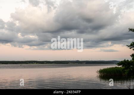 Des nuages puissants au-dessus d'un lac avec des éoliennes à l'horizon Banque D'Images