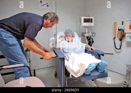 Femme à l'hôpital attendant et étant préparée pour l'opération sur les genoux endommagés blessés par un médecin avec un peu d'électronique et le mari d'heure Banque D'Images