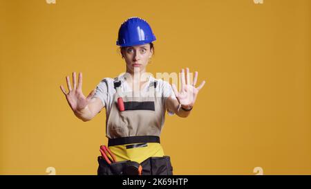 Portrait d'un ouvrier de construction faisant signe d'arrêt avec la paume, la publicité ne passe pas et le geste de finition en studio. Entrepreneur féminin affichant le symbole de fin de délai après avoir travaillé sur la rénovation. Banque D'Images